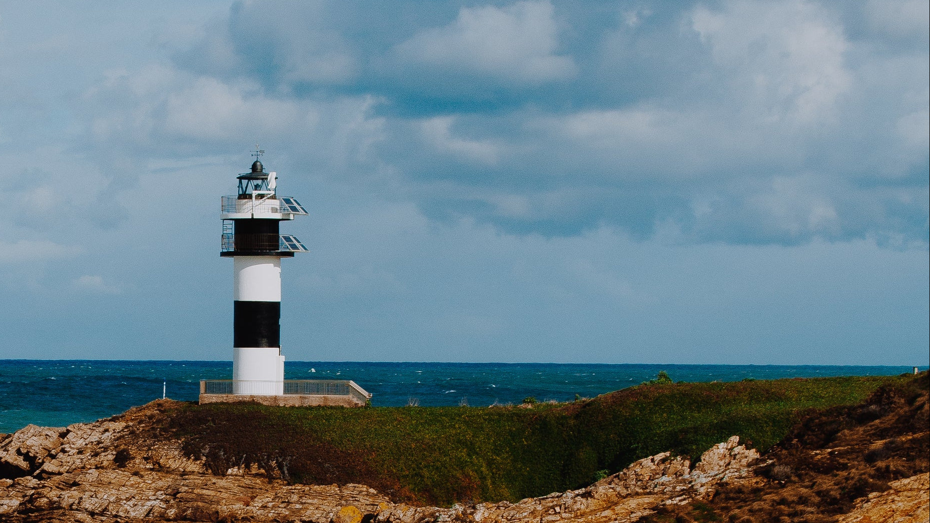 Lighthouse on a rocky outcrop with ocean and cloudy sky in the background